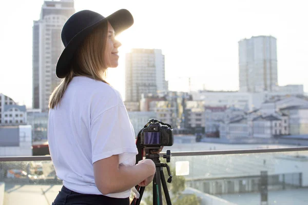 Fotograf dziewczyna z aparatem i statywu na tle miasta, ona fotografie o zachodzie słońca, Kobieta strzela wideo — Zdjęcie stockowe