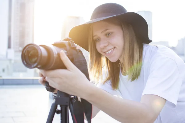 Κορίτσι φωτογράφος με μια κάμερα και ένα τρίποδο σε φόντο της πόλης, φωτογραφίες στο ηλιοβασίλεμα, μια γυναίκα πυροβολεί ένα βίντεο — Φωτογραφία Αρχείου