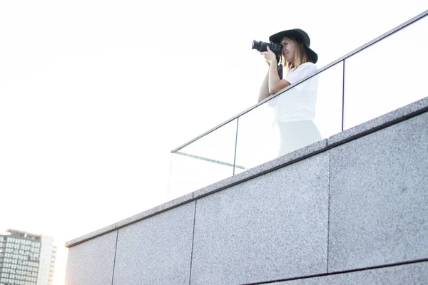 Fille photographe, photographie la ville sur le toit de la maison, une touriste femme regarde du balcon de l'hôtel au coucher du soleil — Photo