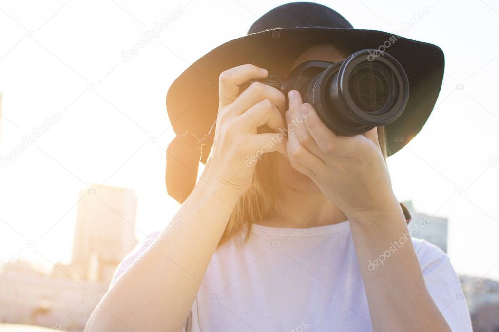 portrait of a girl photographer, a woman with a modern camera photographs against the backdrop of a city sunset