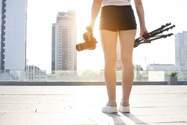 Młoda dziewczyna fotograf z aparatem i statywu na tle miasta, ona fotografie zachód słońca — Zdjęcie stockowe