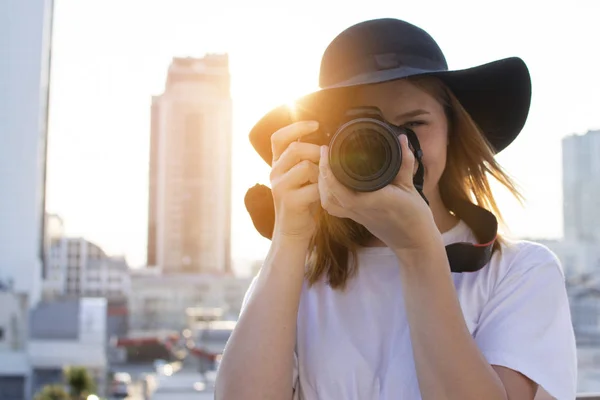 Porträt einer Fotografin, eine Frau mit einer modernen Kamera fotografiert vor dem Hintergrund eines städtischen Sonnenuntergangs — Stockfoto