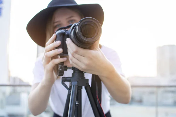 Fotógrafa con una cámara y un trípode sobre un fondo de la ciudad, fotografía al atardecer, una mujer graba un vídeo —  Fotos de Stock