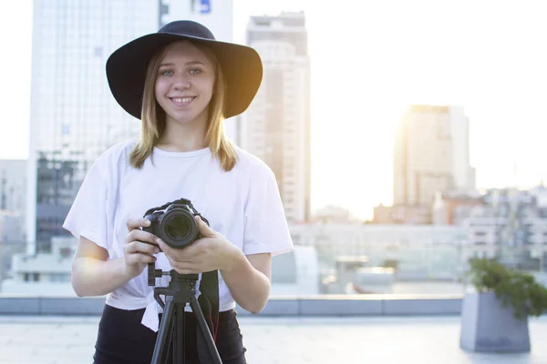 街の背景にカメラと三脚を持つ女の子の写真家、彼女は日没時に写真を撮る、女性はビデオを撮影 — ストック写真