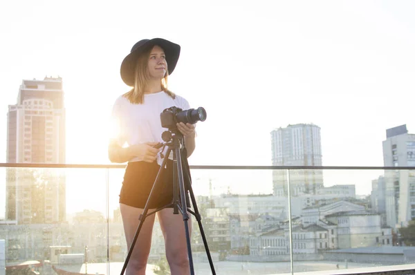 Fotograf dziewczyna z aparatem i statywu na tle miasta, ona fotografie o zachodzie słońca, Kobieta strzela wideo — Zdjęcie stockowe