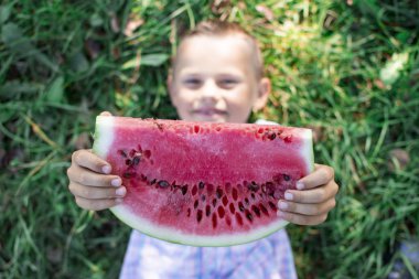 çocuk yeşil çim enyatıyor ve karpuz büyük bir parça tutar, küçük bir öğrenci güneşli bir yaz gününde bir karpuz yiyor, kopya alan