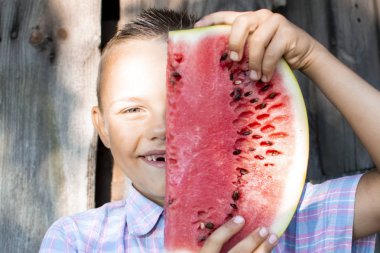 çocuk ahşap bir kırsal duvara karşı karpuz büyük bir parça tutar, küçük bir okul çocuğu güneşli bir yaz gününde bir kamera yerine bir karpuz fotoğrafları, yakın çekim