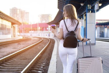 çekici kız istasyonda bagaj ile ayakta ve tren bekliyor, öğrenci bir geziye gidiyor, o kahve ile platform boyunca yürüyor, kopya alanı
