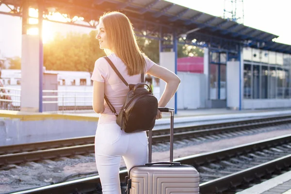 girl stands on the platform of the station with a suitcase and waits for a train, a student travels, leaves for summer vacation, copy space