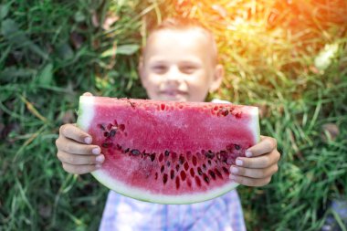 çocuk yeşil çim enyatıyor ve karpuz büyük bir parça tutar, küçük bir öğrenci güneşli bir yaz gününde bir karpuz yiyor, kopya alan