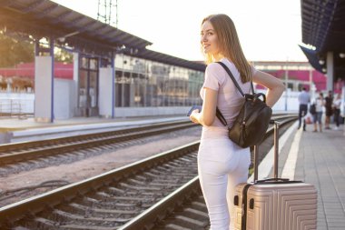 çekici kız istasyonda bagaj ile ayakta ve tren bekliyor, trenin arka planına karşı bir öğrencinin portresi, kopya alanı