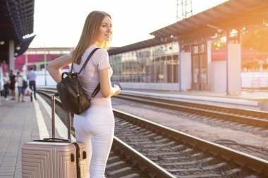 kız bir bavul ile istasyonun platformu üzerinde duruyor ve bir tren bekliyor, bir öğrenci seyahat, yaz tatili için bırakır, kopya alanı