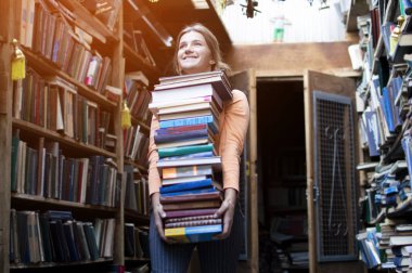 kız öğrenci kitap büyük bir yığın tutar ve kütüphanede edebiyat bir sürü taşır, o çalışma için hazırlanıyor, kitap satıcısı bir kitapçı arka plan karşı birçok kitap aldı