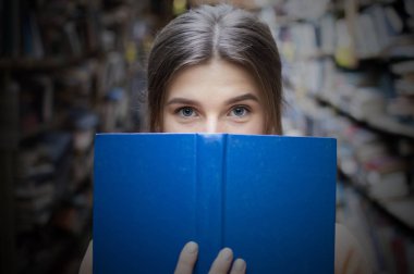 kız öğrenci kütüphanede büyük bir mavi kitap okur ve kameraya bakar, o mavi gözleri, yakın çekim var
