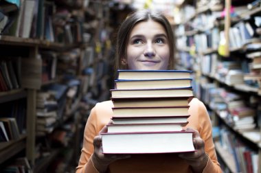 kız öğrenci kütüphanede kitap yığını tutar, o edebiyat arar ve okumak için teklif, bir kadın çalışma için hazırlar, bilgi güç, kitapçı arka planda kitapçı, kibir