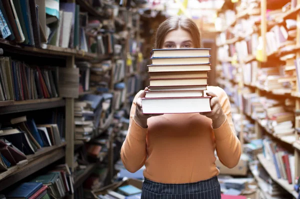 Fille étudiante détient une pile de livres dans la bibliothèque, elle recherche de la littérature et offre de lire, une femme se prépare pour l'étude, la connaissance est le pouvoir, libraire sur le fond de la librairie, conce — Photo