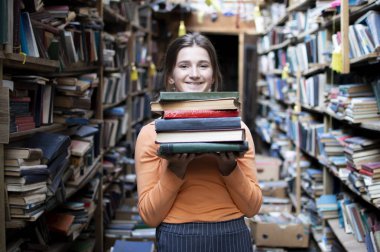 kız öğrenci kütüphanede kitap yığını tutar, o edebiyat arar ve okumak için teklif, bir kadın çalışma için hazırlar, bilgi güç, kavram kitapçı