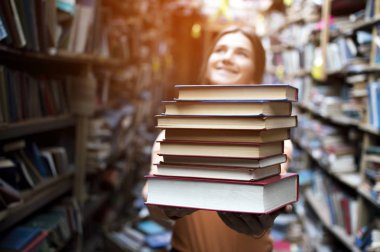 kız öğrenci kütüphanede kitap yığını tutar, o edebiyat arar ve okumak için teklif, bir kadın çalışma için hazırlar, bilgi güç, kitapçı arka planda kitapçı, kibir