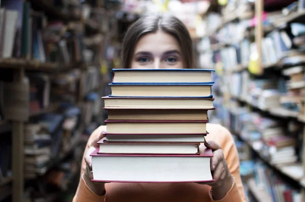 Девушка студентка держит стопку книг в библиотеке, она ищет литературу и предлагает читать, женщина готовится к учебе, знания сила, книготорговец на фоне книжного магазина, conce — стоковое фото