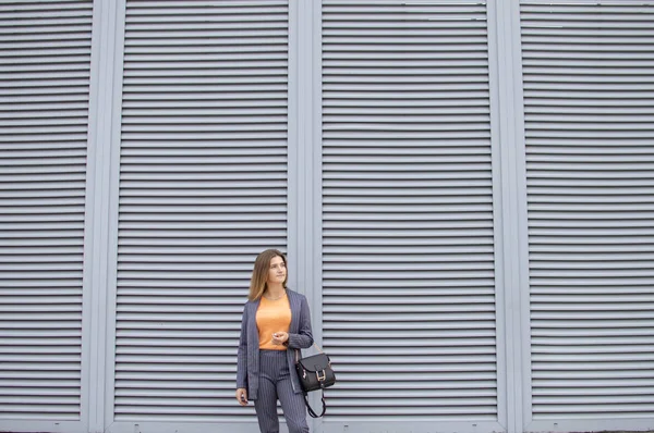Деловая женщина в утреннем пребывании в городе на фоне стены, девушка в полосатом костюме гуляет по улице — стоковое фото