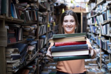 kız öğrenci kütüphanede kitap yığını tutar, o edebiyat arar ve okumak için teklif, bir kadın çalışma için hazırlar, bilgi güç, kavram kitapçı
