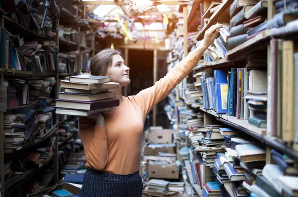 Девушка студентка ищет литературу в старой библиотеке, она берет книгу с книжной полки, женщина ищет информацию в архивах — стоковое фото