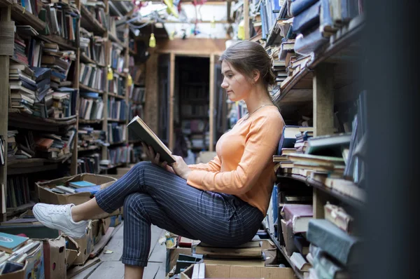 Девушка студентка читает книгу в библиотеке, женщина любит много читать, она ищет литературу на книжных полках, знания сила, понятие — стоковое фото