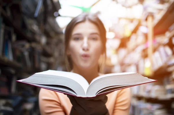 Fille étudiante lit un grand vieux livre dans la bibliothèque et souffle de la poussière, gros plan — Photo