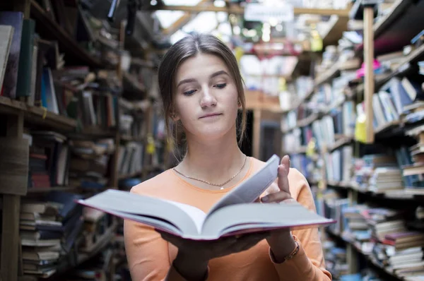 Fille étudiante lit un livre dans la bibliothèque, elle tourne les pages et brosse des informations — Photo