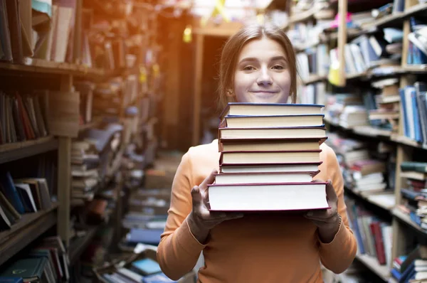 kız öğrenci kütüphanede kitap yığını tutar, o edebiyat arar ve okumak için teklif, bir kadın çalışma için hazırlar, bilgi güç, kitapçı arka planda kitapçı, kibir