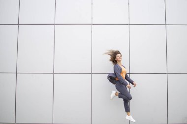 enerjik kız öğrenci sokakta gri bir duvara karşı atlar, şık kadın bir mola dansları