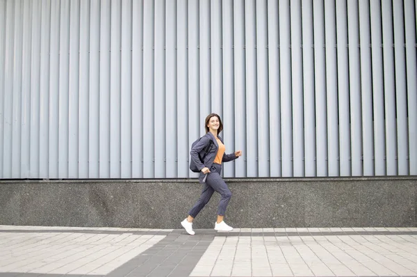 Uczeń dziewczyna biegnie do szkoły na tle ściany na ulicy, kobieta jest późno do pracy — Zdjęcie stockowe