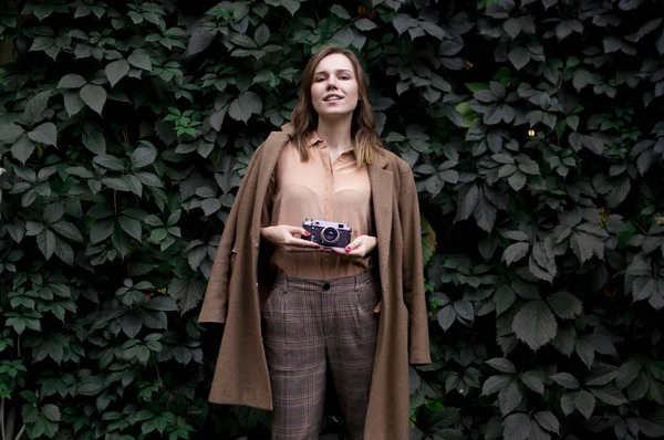 Jovem fotógrafo fica com uma câmera de filme perto de uma parede de folhas na floresta, uma mulher fotografa na natureza — Fotografia de Stock