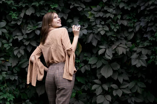 Молодая девушка фотограф стоит с кинокамерой рядом со стеной листьев в лесу, женщина фотографирует в природе — стоковое фото