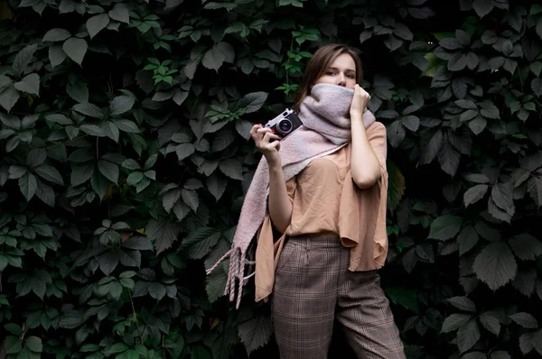 Молодая девушка фотограф стоит с кинокамерой рядом со стеной листьев в лесу, женщина фотографирует в природе — стоковое фото