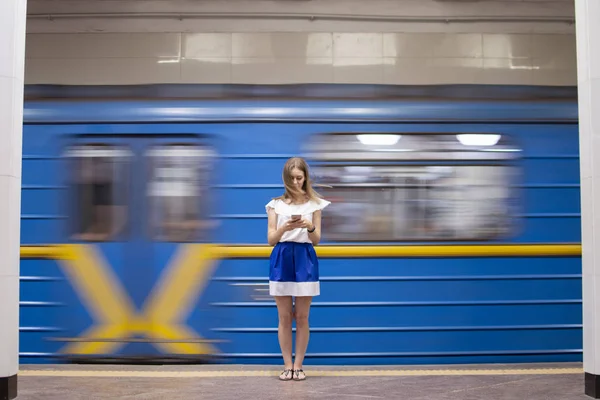 Girl stands on a subway platform and listens to music on the background of a passing train, a student uses a phone in the subway, copy space — Stock Photo, Image