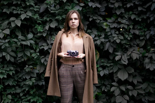 Jovem fotógrafo fica com uma câmera de filme perto de uma parede de folhas na floresta, uma mulher fotografa na natureza — Fotografia de Stock