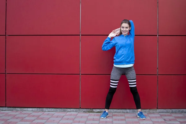sporty girl is training against a red wall in the street, a woman is doing warm-up in sportswear outdoors, copy space