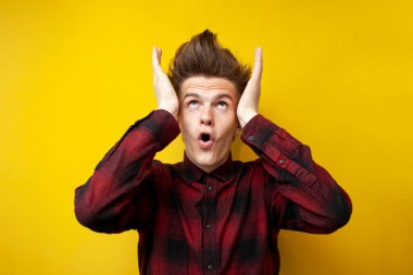 Şok olmuş genç adam saçına dokunuyor ve sarı izole edilmiş arka planda merak ediyor. Kuaförlü hippi öğrenci saçını kestiriyor.