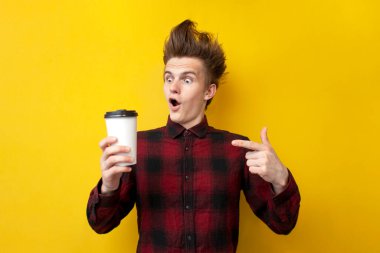 Şaşırmış bir adam sarı izole edilmiş bir arka planda enerji kahvesi içiyor. Komik saç stili olan bir adam canlandırıcı bir içki tutuyor.