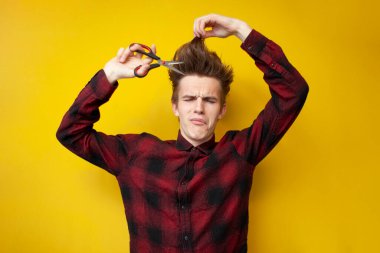 Komik saç stili olan genç üzgün adam uzun saçlarını kesiyor ve sarı izole bir arka planda ağlıyor, mutsuz hippi saç stilini değiştiriyor.