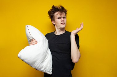 Yastıklı yorgun ve uykulu öğrenci, sarı izole bir arka planda üzgün. Adamın uyku sorunu var.