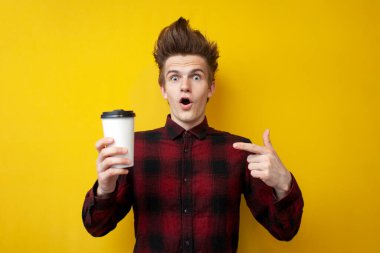 Genç şokta olan adam canlandırıcı kahve içiyor ve sarı izole bir arka plana şaşırıyor. Bir adam enerji içeceği içiyor.