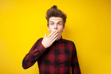 Genç şokta olan adam, elleri sarı izole bir arka planda ağzını kapatıyor, korkmuş adam şaşırıyor.