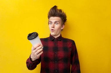 Şaşırmış bir adam sarı izole edilmiş bir arka planda enerji kahvesi içiyor. Komik saç stili olan bir adam canlandırıcı bir içki tutuyor.