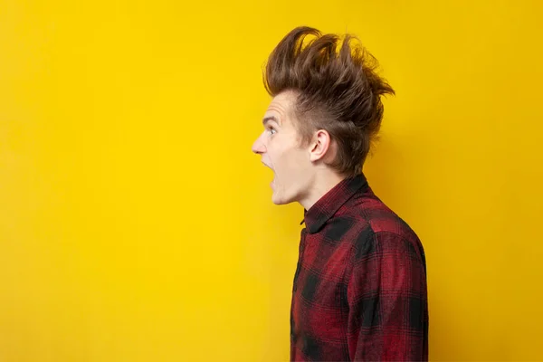 young shocked guy screaming on a yellow isolated background, hipster with a funny hairstyle is panicking, close-up