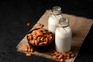 iki şişe badem sütü koyu siyah bir masada fındıklı, vejetaryen sütü şekersiz ve laktozsuz, kopyalama alanı