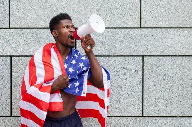 Amerikan bayrağı taşıyan Afro-Amerikan bir adam megafonla bağırıyor ve şehrin arka planına karşı protestolar düzenliyor. Siyahların hayatı kavram meselesidir.