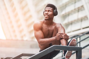 Afro-Amerikan atletizm sporcusu yazın fotokopi odasına bakıyor tişörtsüz bir sporcu ve müzik dinliyor.