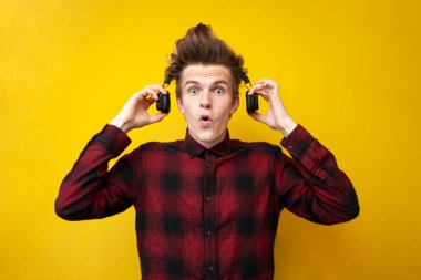 Sarı izole edilmiş arka planda kablosuz kulaklıklı şok olmuş genç adam, hipster müzik dinler ve şaşırır.